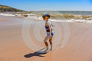 Little boy on anjuna beach with yellow sand, blue ocean and waves. North Goa, India. March 12, 2020.