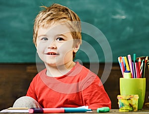 Little boy at art lesson. Smiling blond boy sitting at the desk with his knee bent