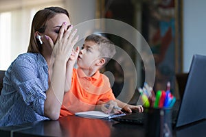 Little boy asking tired mother at home office during online job