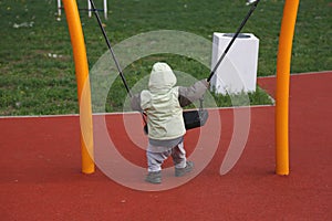 Little boy in autumn jacket swinging on swing