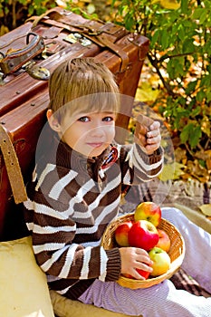 Little boy in autumn park with a suitcase, chocolate and apples