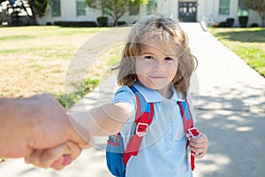 Little boy with backpack holding parent fathers hand on blurred school building background. Child with rucksacks