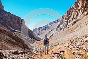 little boy with a backpack stands along the path against the backdrop of the mountains. travel with children to the mountains.