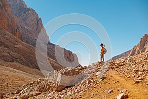 little boy with a backpack stands along the path against the backdrop of the mountains. travel with children to the mountains.