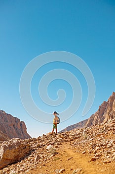 little boy with a backpack stands along the path against the backdrop of the mountains. travel with children to the mountains.