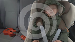 Little boy in the backseat of a car. The car is going on a bad road. Travel with baby. Sleeping kid with a guitar.