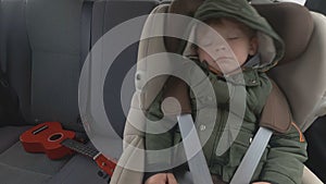 Little boy in the backseat of a car. The car is going on a bad road. Travel with baby. Sleeping kid with a guitar.