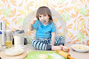 Little boy bakes sitting on a table at home kitchen