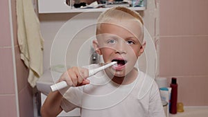 A little boy in the bathroom, he brushes his teeth with an electric toothbrush.