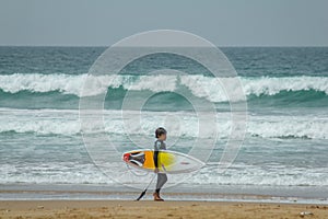 Little boy at the beach with yellow surfboard on the Atlantic Ocean with waves