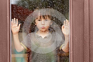 Little boy behind the window in the rain