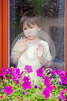 Little boy behind the window in the rain