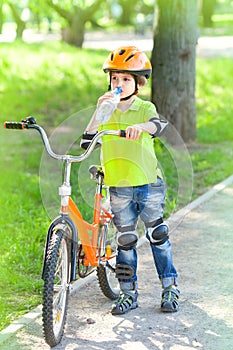 A little boy with a Bicycle drinks water