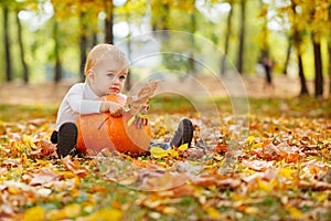 Little boy with big orange pumpkin in hands sitting on the gras