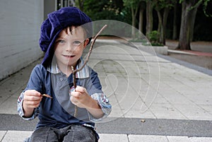 Little boy with big violet cap plays with a piece of a branch
