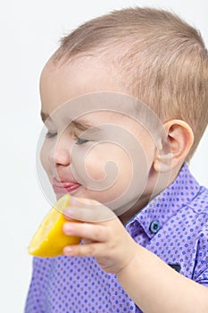 Little boy bites juicy sour lemon white