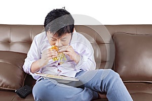 Little boy biting cheeseburger on sofa