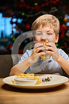 Little boy biting sandwich in festive restaurant sitting New Year celebration