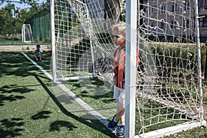 Little boy in black and orange soccer form playing football on open field in yard, young goalkeeper