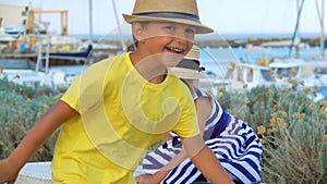 Little boy and blond girl in straw hats are playing catch-up on the quay