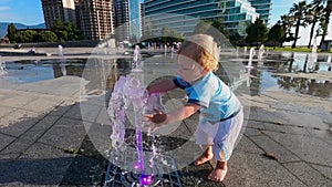 little boy blonde wets his hands in the fountain