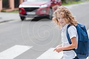 Little boy with a blue backpack crosses the street