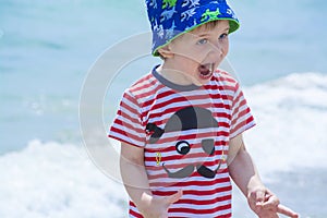 Little boy with blue eyes screaming with happiness on the beach, hamming, photo