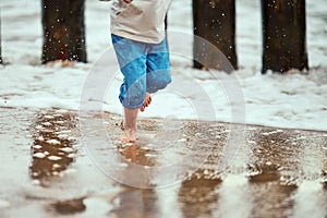 Little boy in blue pants running on sea coast and playing with sea waves, defocused blurred legs