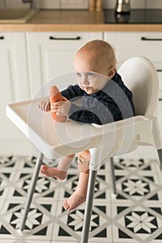 Little boy in a blue t-shirt sitting in a child& x27;s chair eating carrot - baby care and infant child feeding concept