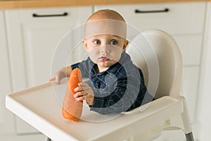 Little boy in a blue t-shirt sitting in a child's chair eating carrot copy space and empty space for text - baby