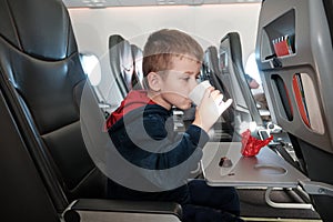 A little boy on board the plane eats chocolate candies while drinking water