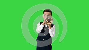 Little boy in a bow tie playing the trumpet and looking at camera on a Green Screen, Chroma Key.