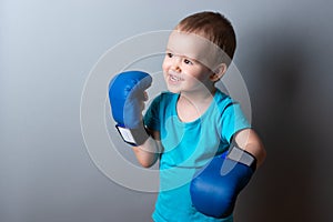 a little boy in boxing gloves and a blue T-shirt on a gray background.expression of emotions.copy space.
