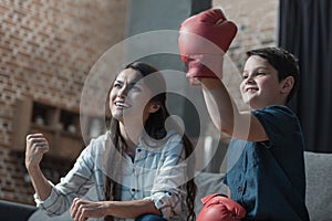 Little boy in boxing gloves and his mother cheering while watching boxing match