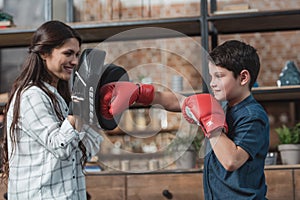 Little boy in boxing gloves kicking a punching pad held