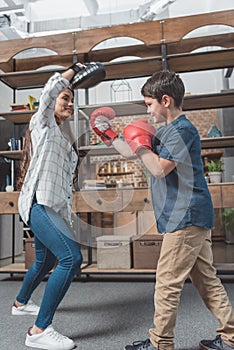 Little boy in boxing gloves kicking a punching pad held by his mother