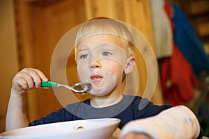 Little boy with a broken wrist eating at the table. Boy with a plaster on his arm