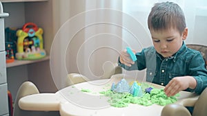 A little boy builds castles and various figures of green kinetic sand