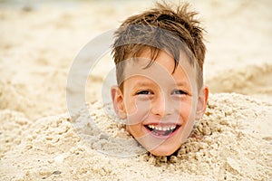 Little boy buried in the sand on beach