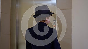 Little boy in business suit, hat and briefcase comes into elevator back view. Businessman pushing button for calling