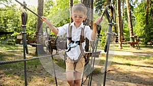 Little boy carefully walking over cable or rope between two trees in park. Active childhood, healthy lifestyle, kids playing