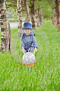 Little boy carries plastic wheelbarrow loaded with