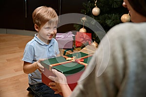 Little boy celebrates Christmas with mother sharing presents near the X-mas tree