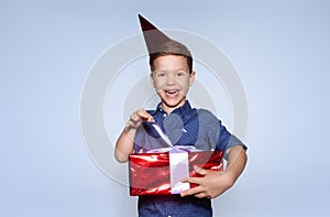 little boy celebrating birthday, wearing party cone, holding red gift.