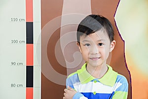 Little boy checking his height at school with measuring height scale on the wall by himself.Smiling cute asia boy measures his