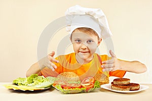 Little boy in chef hat at table with ingredients for hamburger