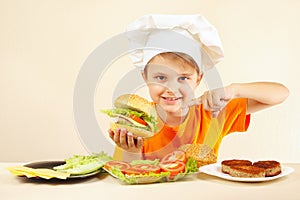 Little boy in chefs hat expressive enjoys cooked hamburger