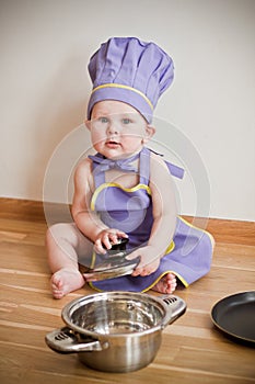 Little boy in a chief hat and aprons sitting on a floor