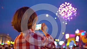 Little boy child filming pictures of beautiful fireworks in night sky display of mobile phone. Hands of baby taking