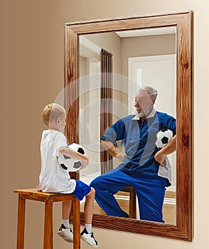 Little boy, child with football ball sitting and looking in mirror with reflection of senior man, Kid in future
